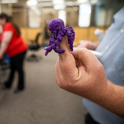 A purple 3D printed octopus with articulating tentacles sits atop a finger in the new Makerspace in King Library
